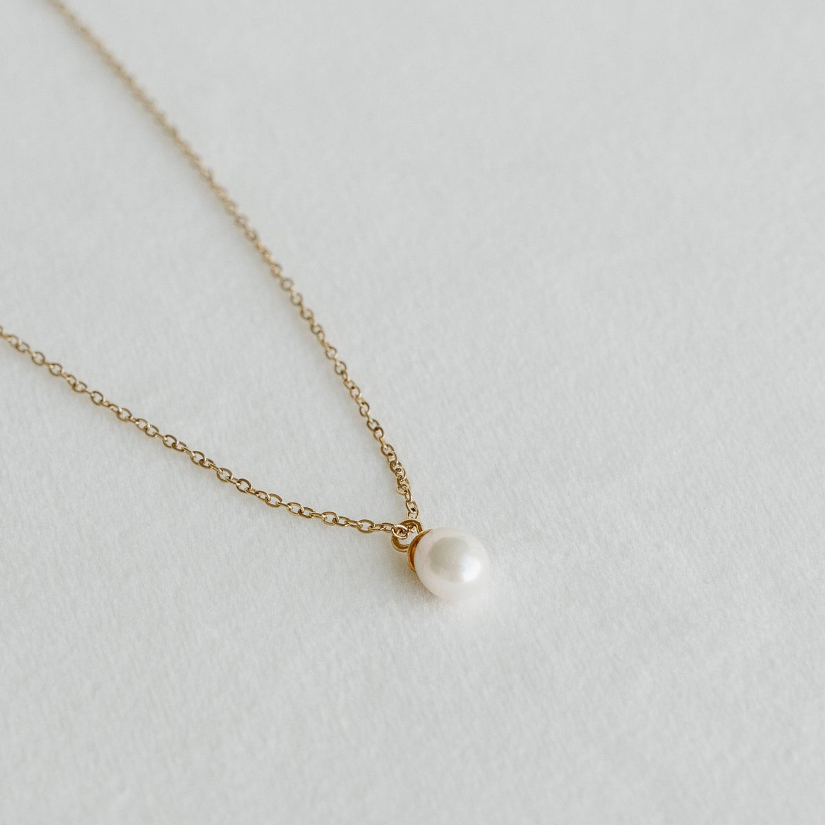 Freshwater pearl pendant on a delicate gold chain necklace laid on a light textured surface - PABOOM