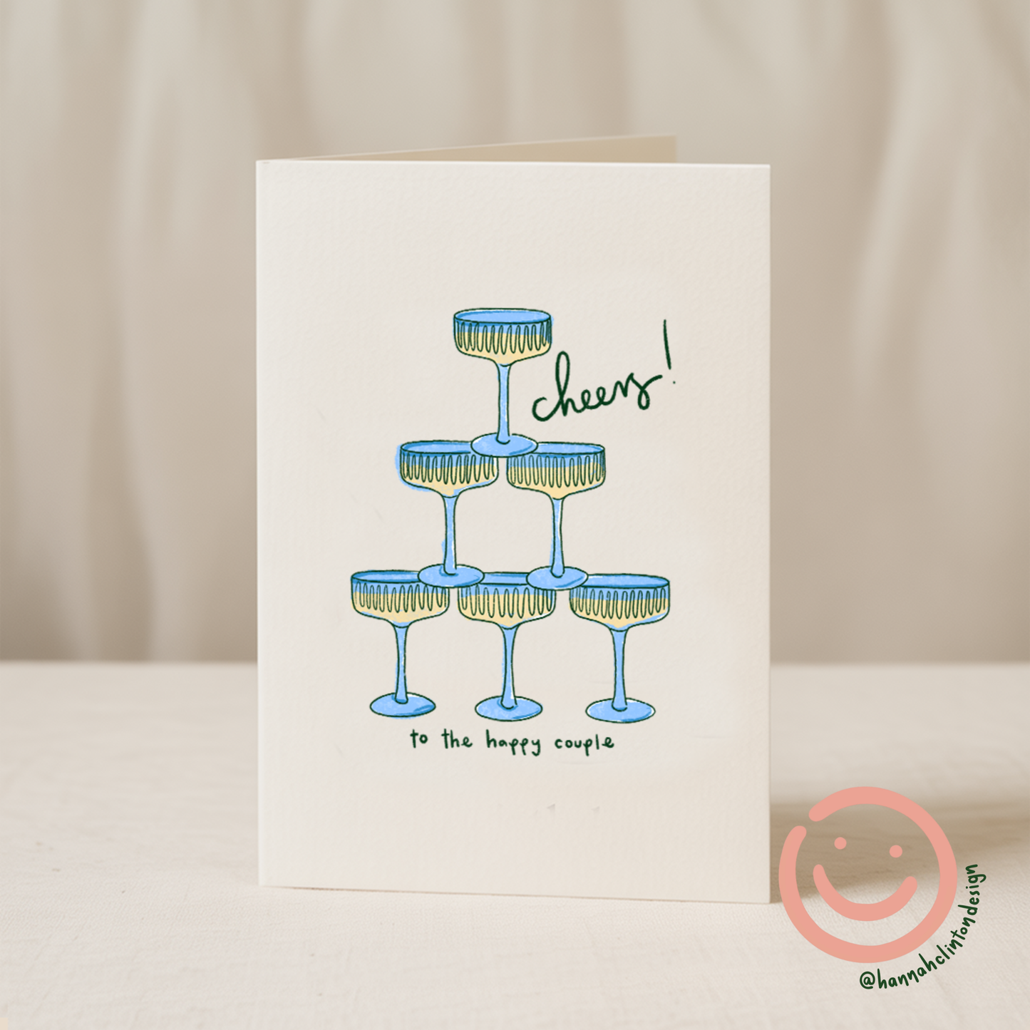 Blue Iris Designs Co wedding card illustrated with a stacked pyramid of blue champagne coupes and "cheers! to the happy couple" text - PABOOM