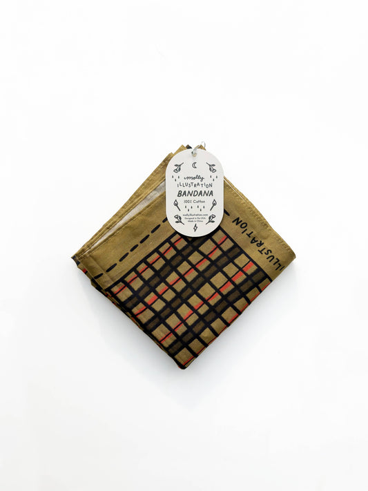 Folded bandana in a gold and brown wonky plaid print with a Molly Illustration branded packaging tag