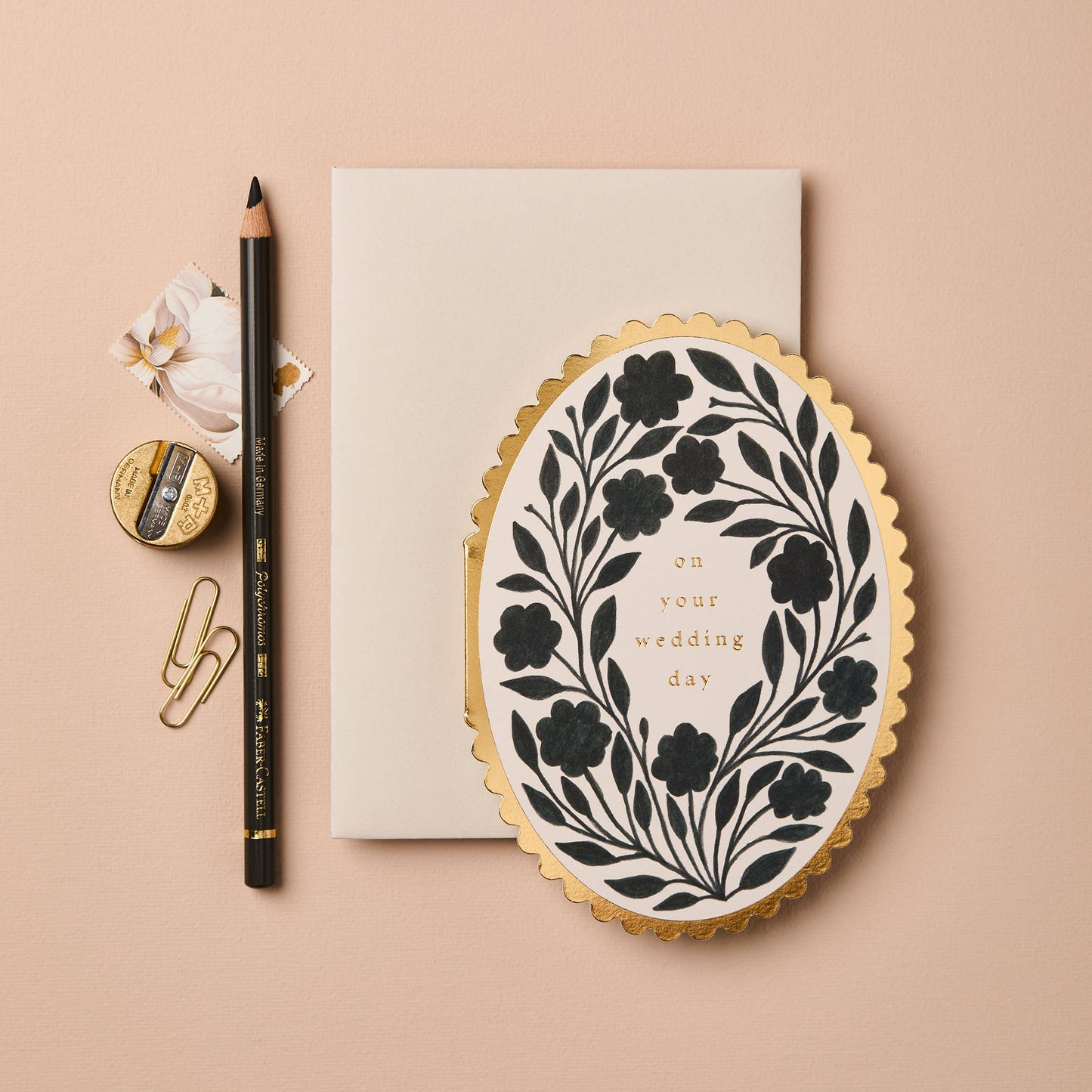 Black floral wreath illustration on oval card with gold scalloped edge, reading On Your Wedding Day