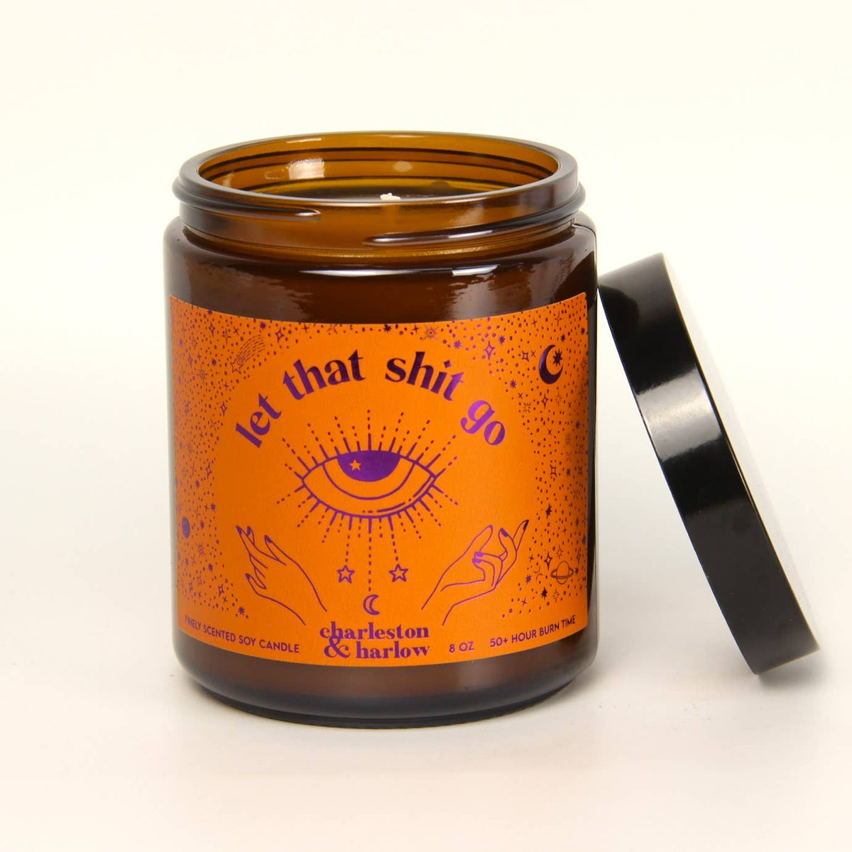 Charleston & Harlow Let That Shit Go soy candle in amber glass jar with orange label featuring a black mystic eye illustration