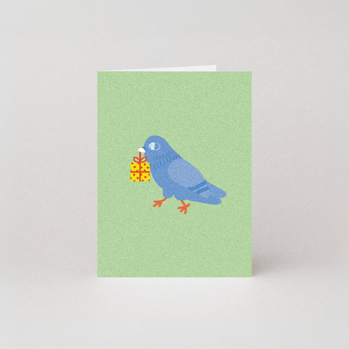 Mini birthday greeting card featuring an illustrated blue pigeon carrying a wrapped yellow gift box in its beak, on a sage green background.