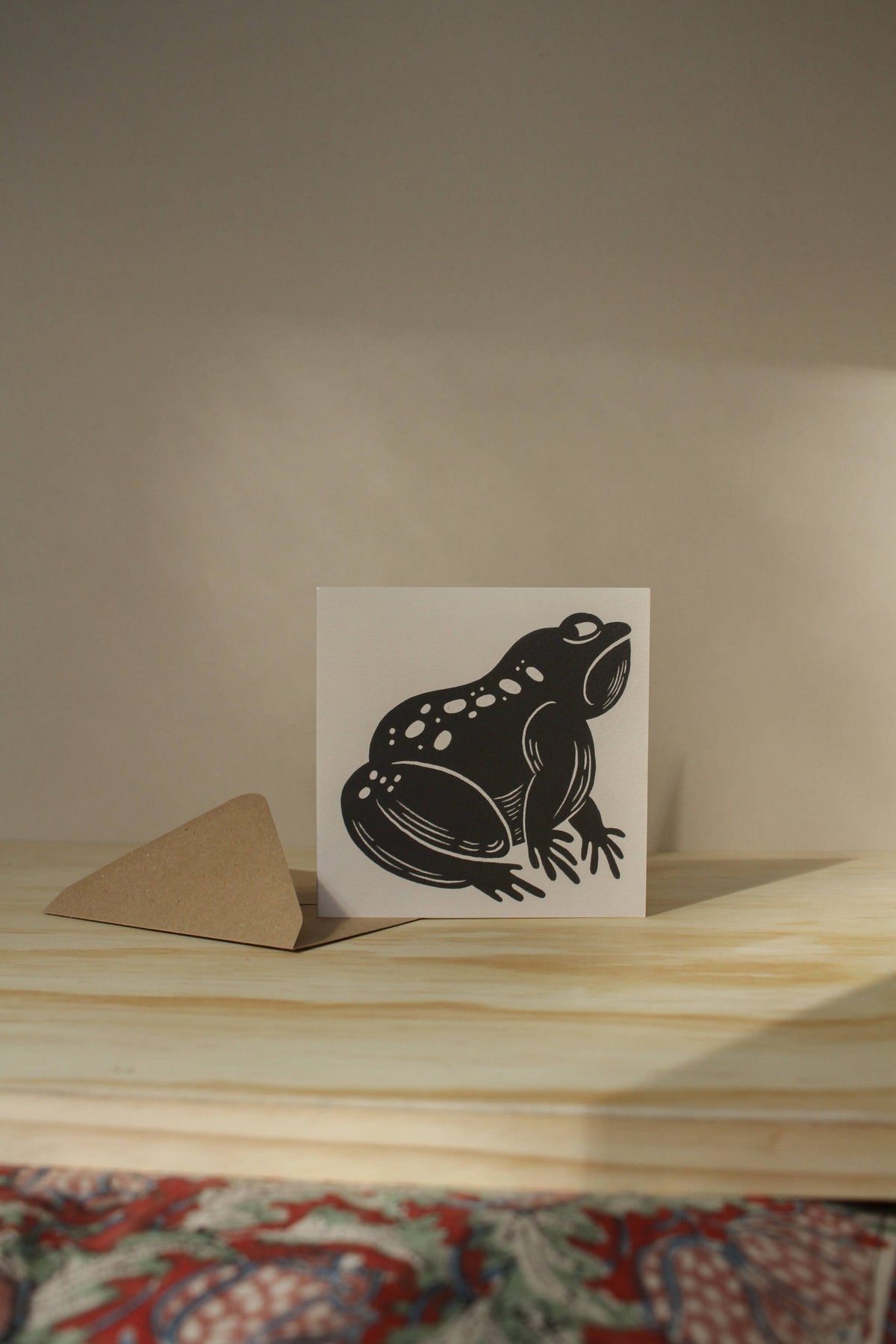 'The Grumpy Frog' card laid flat beside its kraft envelope on a light background