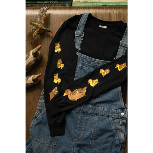 A mama duck and her brood of 3 fluffy ducklings follow the leader down the sleeves of this long sleeve tee. Black, cotton. Worn underneath jean overalls - PABOOM