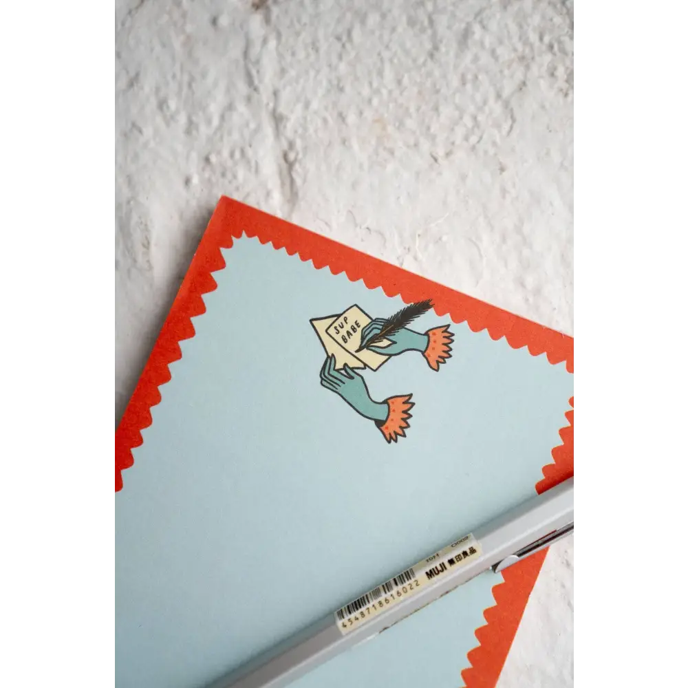 Notepad with a top logo of two hands writing a letter “SUP BABE”. Blue, with red squiggle outline by Stay Home Club | PABOOM