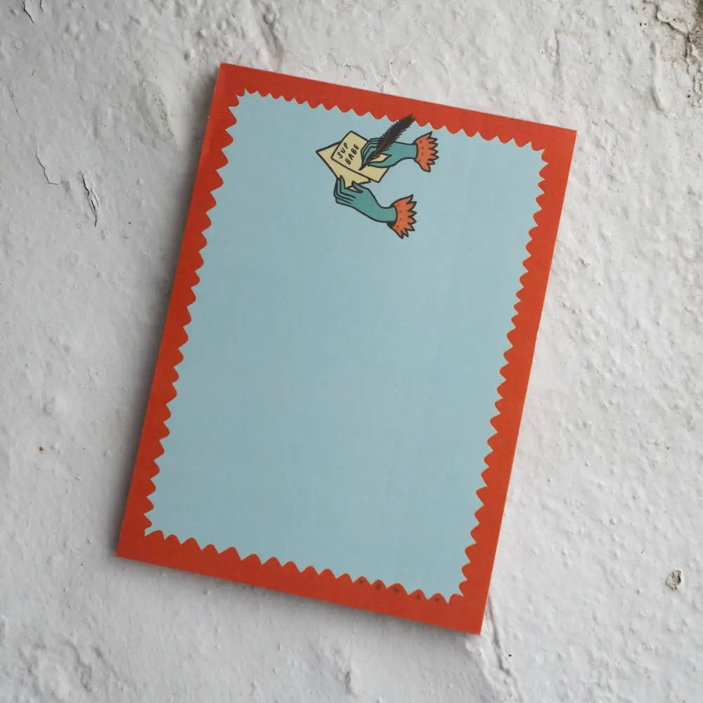 Notepad with a top logo of two hands writing a letter “SUP BABE”. Blue, with red squiggle outline, by Stay Home Club | PABOOM