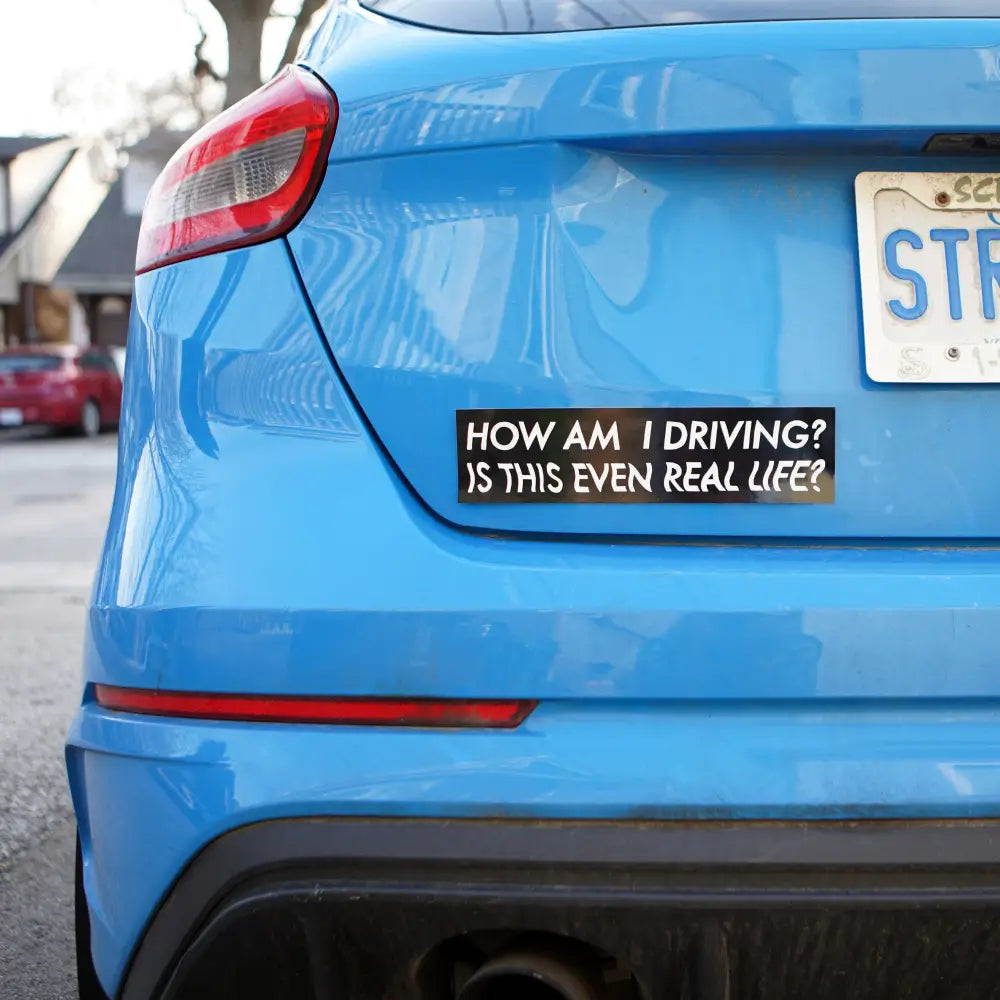 Back of blue car with black bumper sticker with white text "HOW AM I DRIVING? IS THIS EVEN REAL LIFE?" - PABOOM