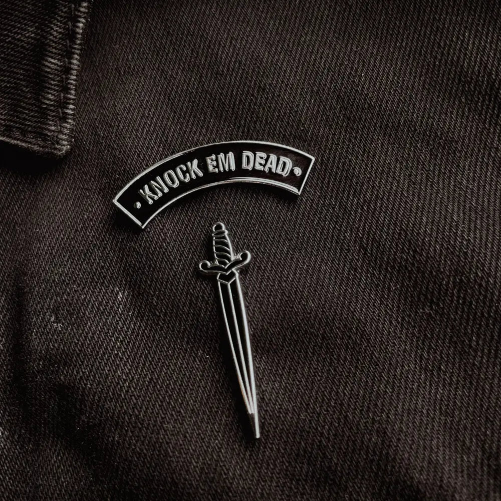 A "knock em dead" and a dagger pin on black jean jacket