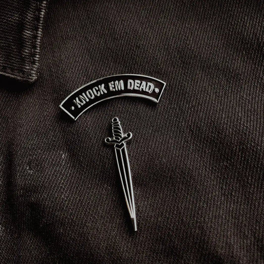 A "knock em dead" and a dagger pin on black jean jacket