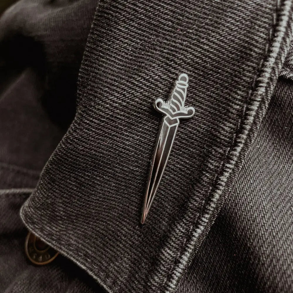a dagger shaped pin on a black jean jacket