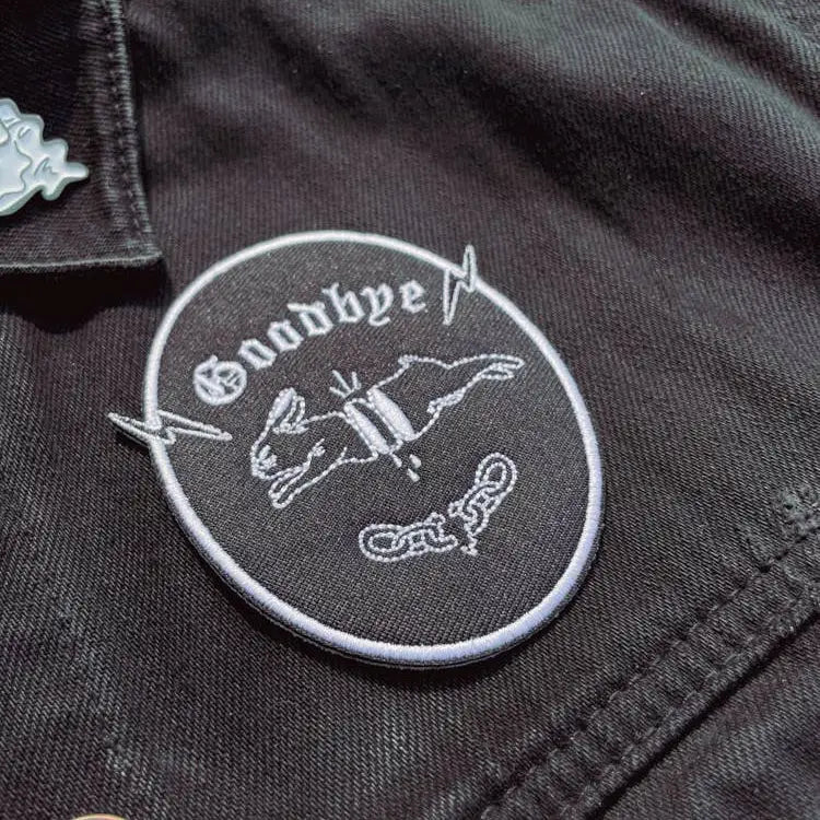 Iron on embroidered patch of a chopped-up rabbit jumping and "goodbye" written underneath. Black with white embroidery. on fabric