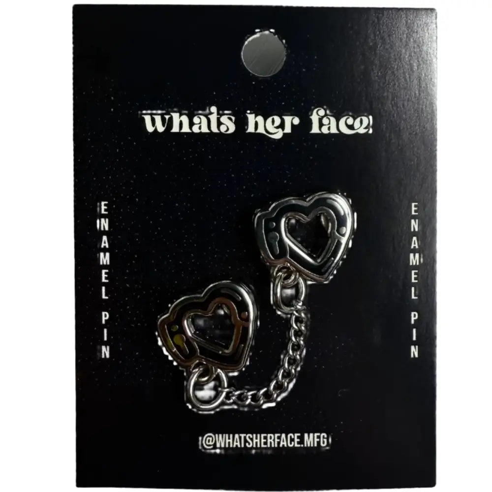 Enamel pin of two hearts connected by a chain handcuffs on cardstock backing