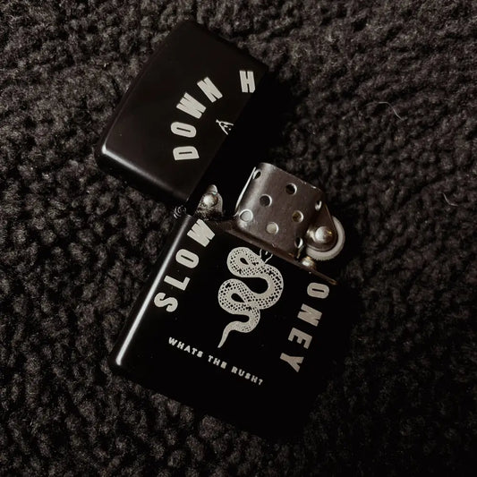 Zippo black lighter with a snake and text SLOW DOWN HONEY whats the rush?, opened on black fabric