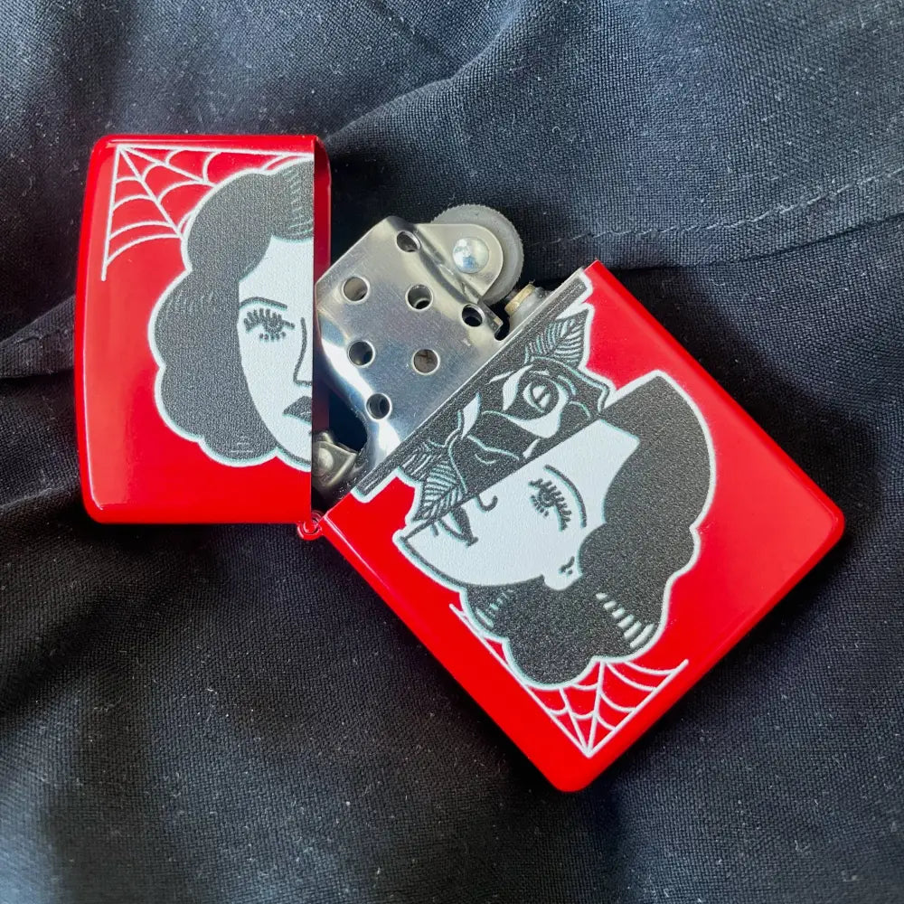Zippo red lighter with a woman’s face splint in half with rose in middle, opened on black fabric