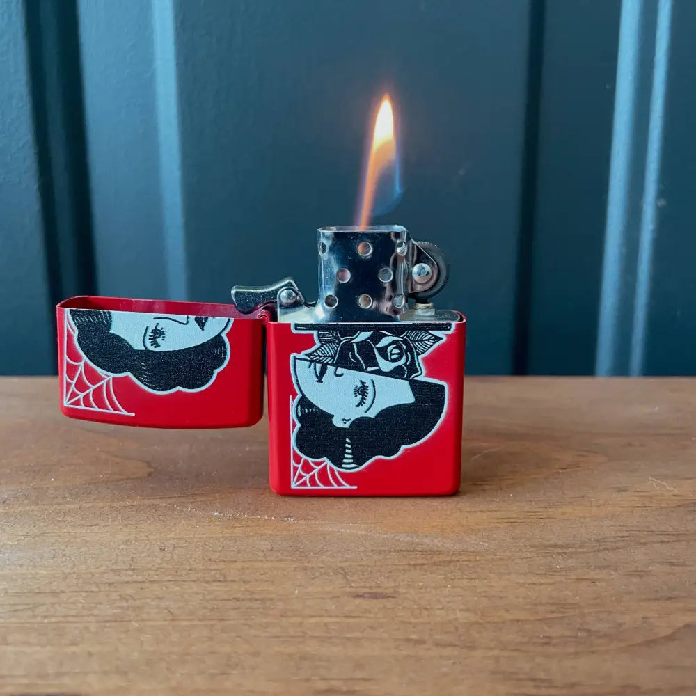 Zippo red lighter with a woman’s face splint in half with rose in middle, opened with flame