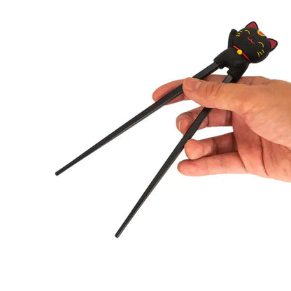 Hand holding black lucky cat training chopsticks with gold whiskers and red collar - PABOOM
