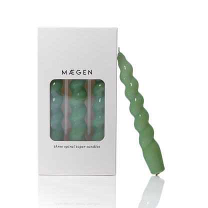 MÆGEN spiral taper candle in sage green leaning against its white branded box printed "three spiral taper candles"