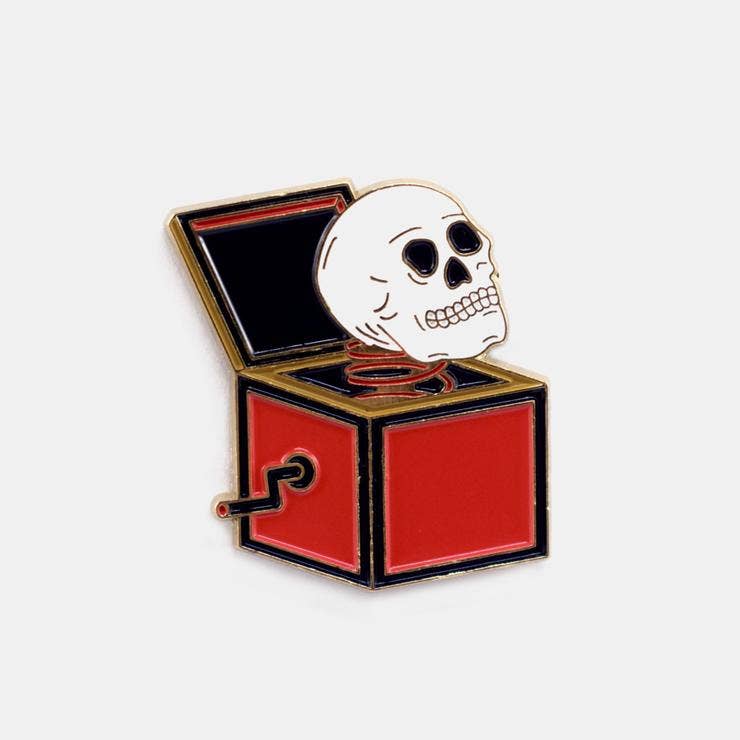 Red and gold enamel pin of a skull popping out of a jack-in-the-box - PABOOM