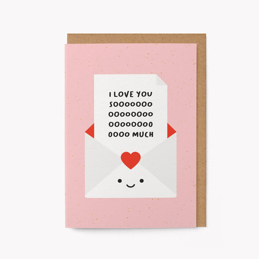 Pink greeting card with an illustrated smiling envelope holding a note that reads 'I love you soooo much,' kraft envelope alongside