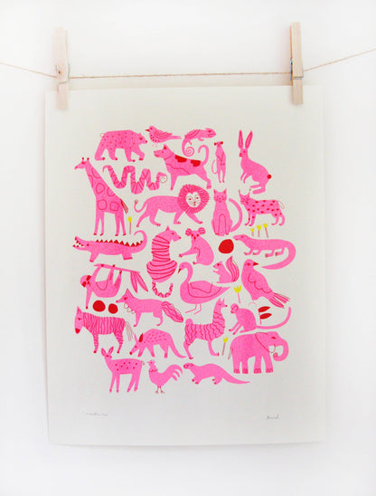 Pink riso print of an animal pattern including lions, zebras, and giraffes on cream paper, clipped to a string — PABOOM