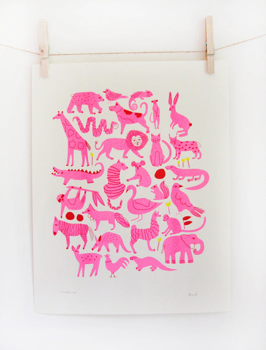 Pink riso print of an animal pattern including lions, zebras, and giraffes on cream paper, clipped to a string — PABOOM