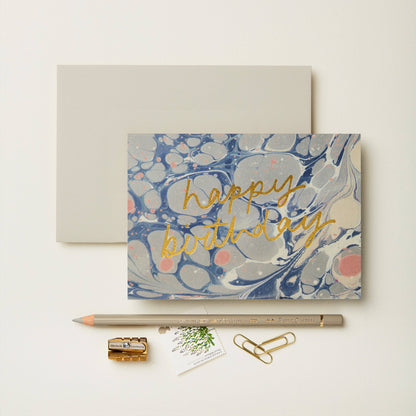 Blue, grey and pink marbled card reading happy birthday in gold script