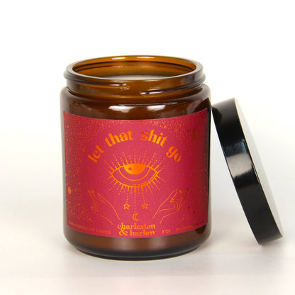 Charleston & Harlow Let That Shit Go soy candle in amber glass jar with dark pink label featuring an orange foil mystic eye illustration