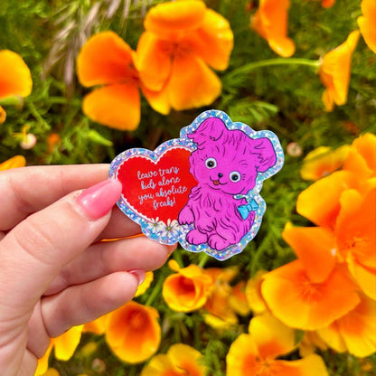 Pink fuzzy vintage-style puppy with a blue bow beside a heart reading leave trans kids alone you absolute freaks!