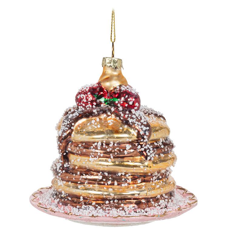 Glass Christmas ornament shaped like a stack of pancakes topped with red berries and a green bow, dusted with glittery white sugar, on a pink glass plate base.