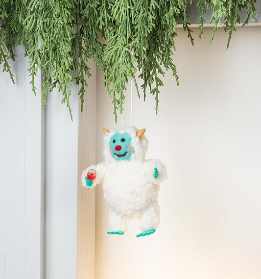 Side view of the felted Yeti Ornament showing its horns and textured wool coat.