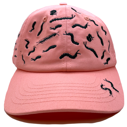 Pink dad hat covered in black embroidered centipede designs scattered across the crown and brim, front view.