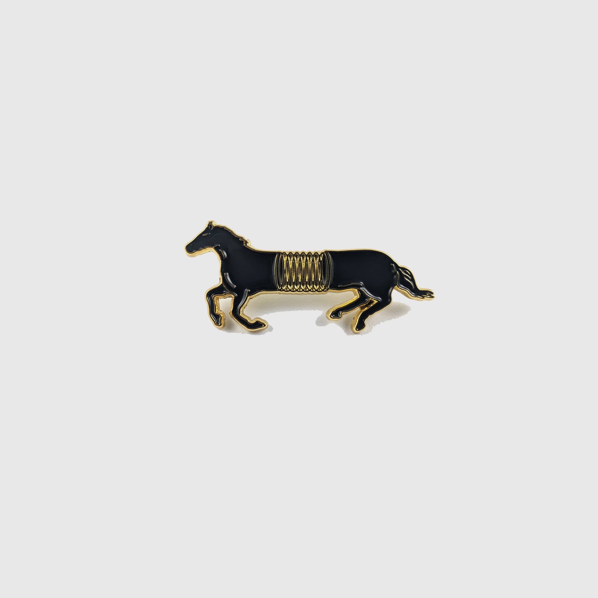 Black and gold enamel pin of a horse mid-gallop with a spring coiled around its middle - PABOOM