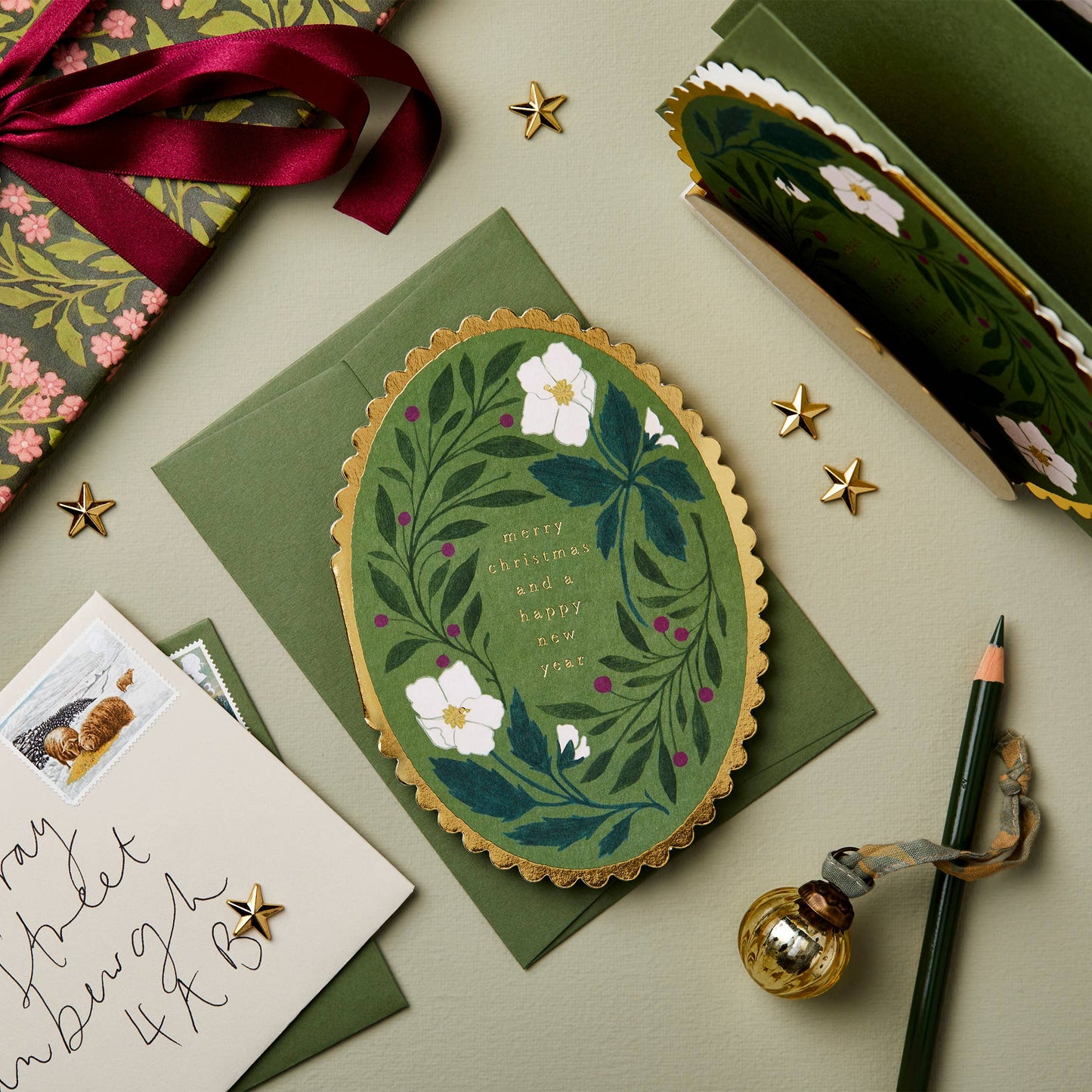 White hellebore flowers and berries on forest green oval card with gold scalloped edge, reading Merry Christmas and a Happy New Year