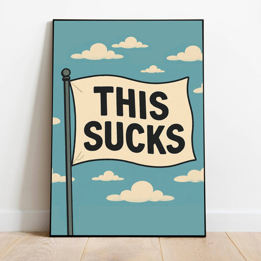 A framed art print leaning against a white wall on a light wood floor. The print features a retro-style illustration of a flag on a pole with the text 'THIS SUCKS' in bold black letters against a light blue sky with cream-colored clouds.