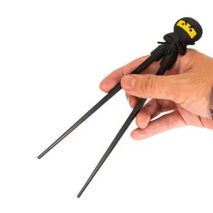 Hand holding black ninja training chopsticks with a yellow-masked silicone ninja topper - PABOOM