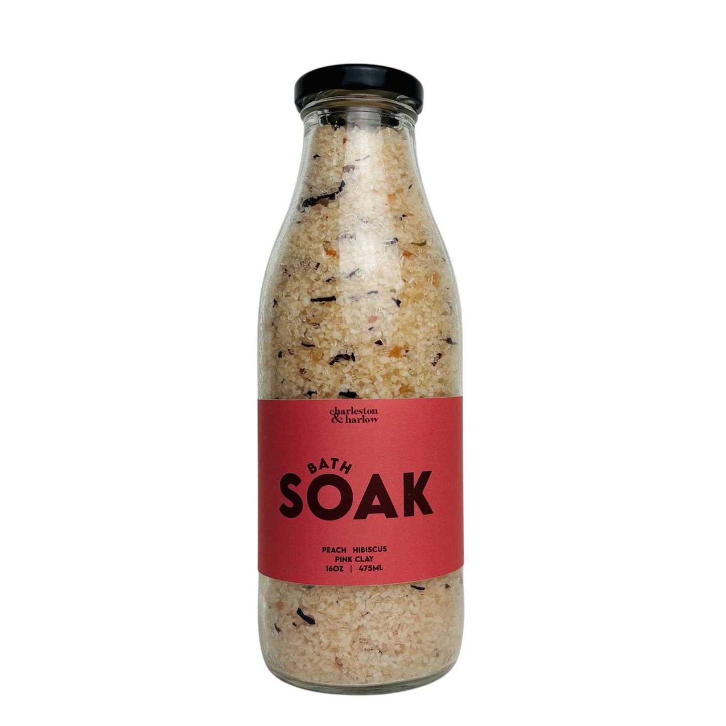 Glass bottle of Charleston & Harlow Bath Soak with red label, peach and hibiscus salt blend with visible petals