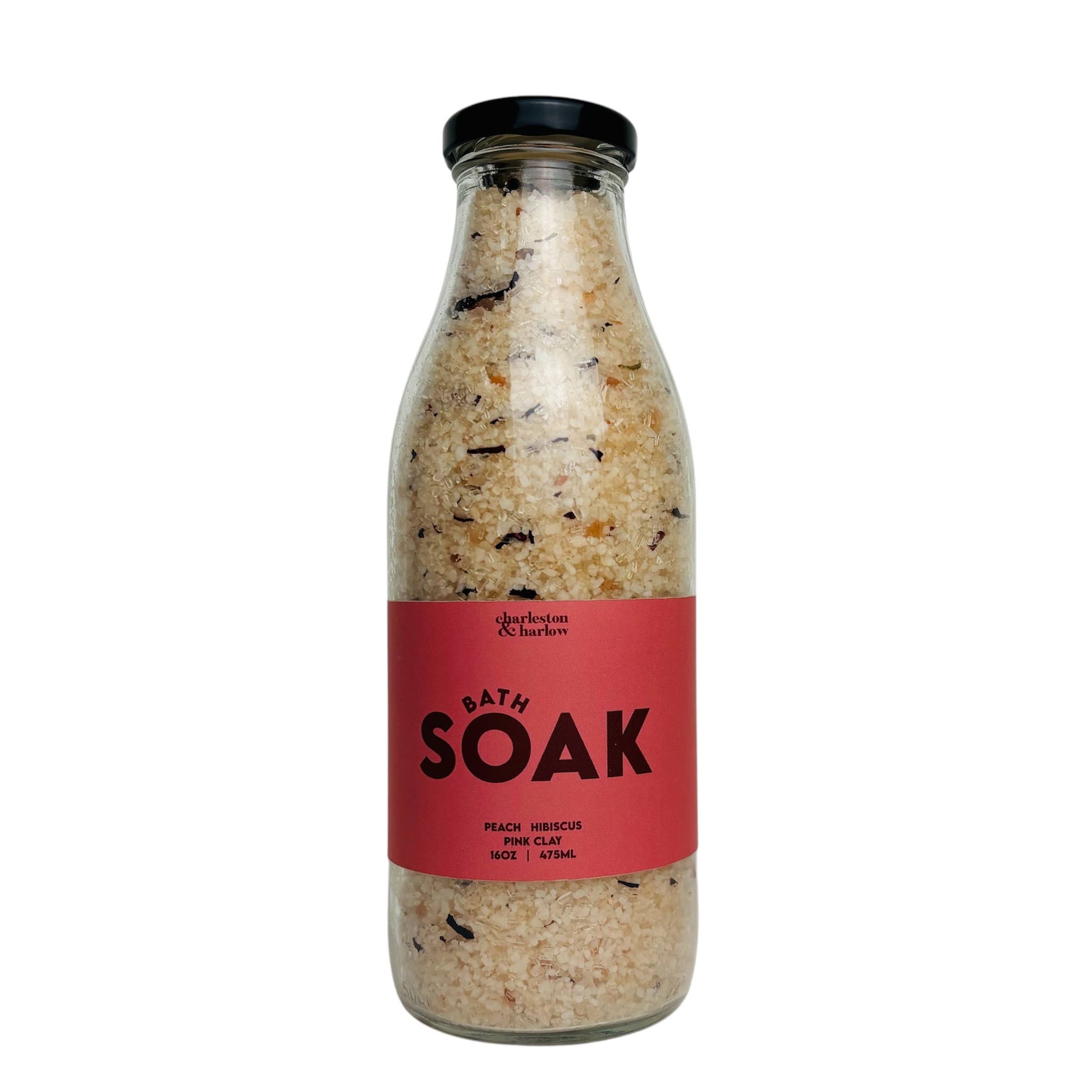 Glass bottle of Charleston & Harlow Bath Soak with red label, peach and hibiscus salt blend with visible petals