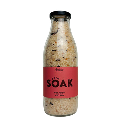 Glass bottle of Charleston & Harlow Bath Soak with red label, peach and hibiscus salt blend with visible petals