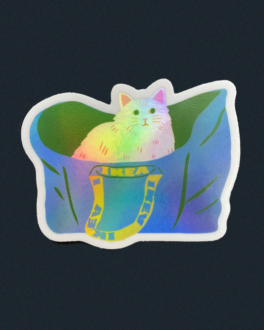 Holographic sticker of a fluffy cat peeking out of a blue IKEA tote bag with leafy greens - PABOOM