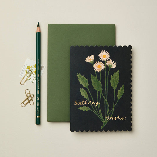 White daisy illustration on inky black scalloped card, reading Birthday Wishes in gold script
