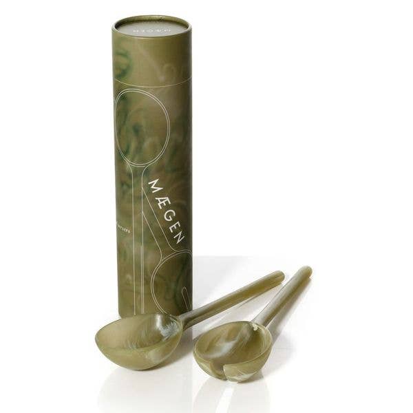 Olive green marbled resin salad server fork and spoon leaning against their MÆGEN cylinder packaging