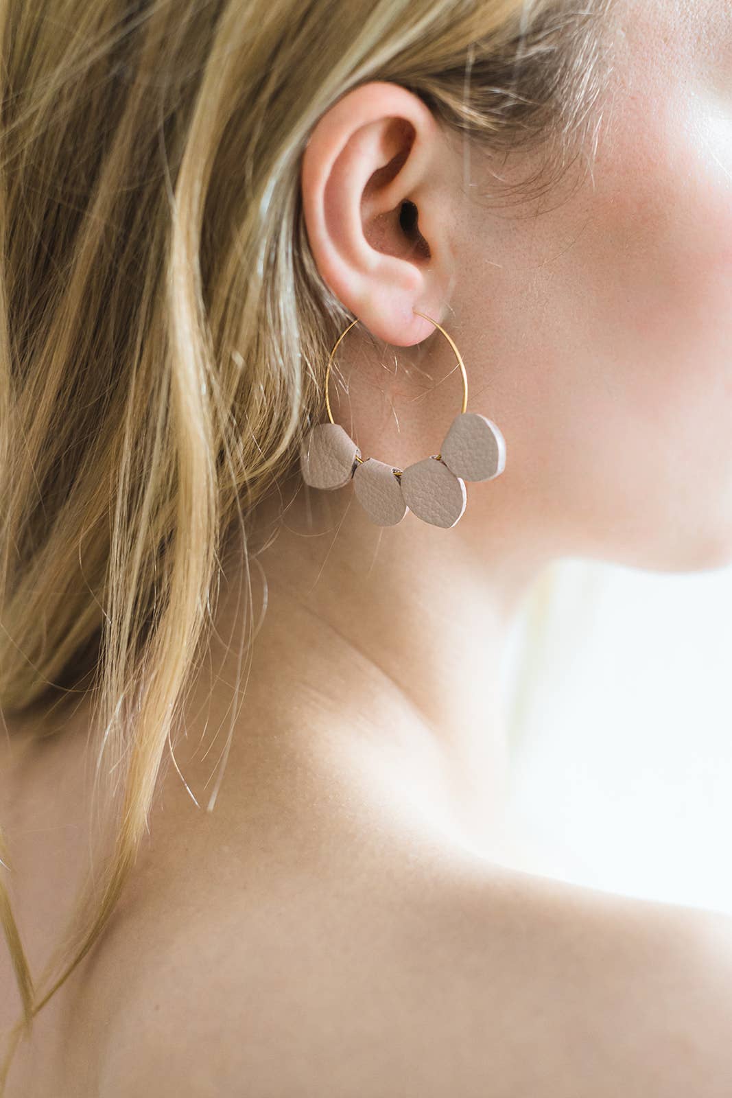 Close-up of model wearing blush pink leather petal hoop earrings