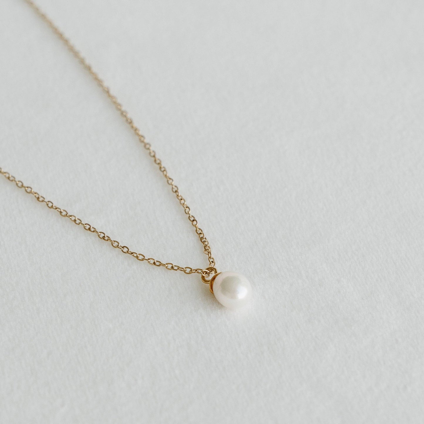 Freshwater pearl pendant on a delicate gold chain necklace laid on a light textured surface - PABOOM