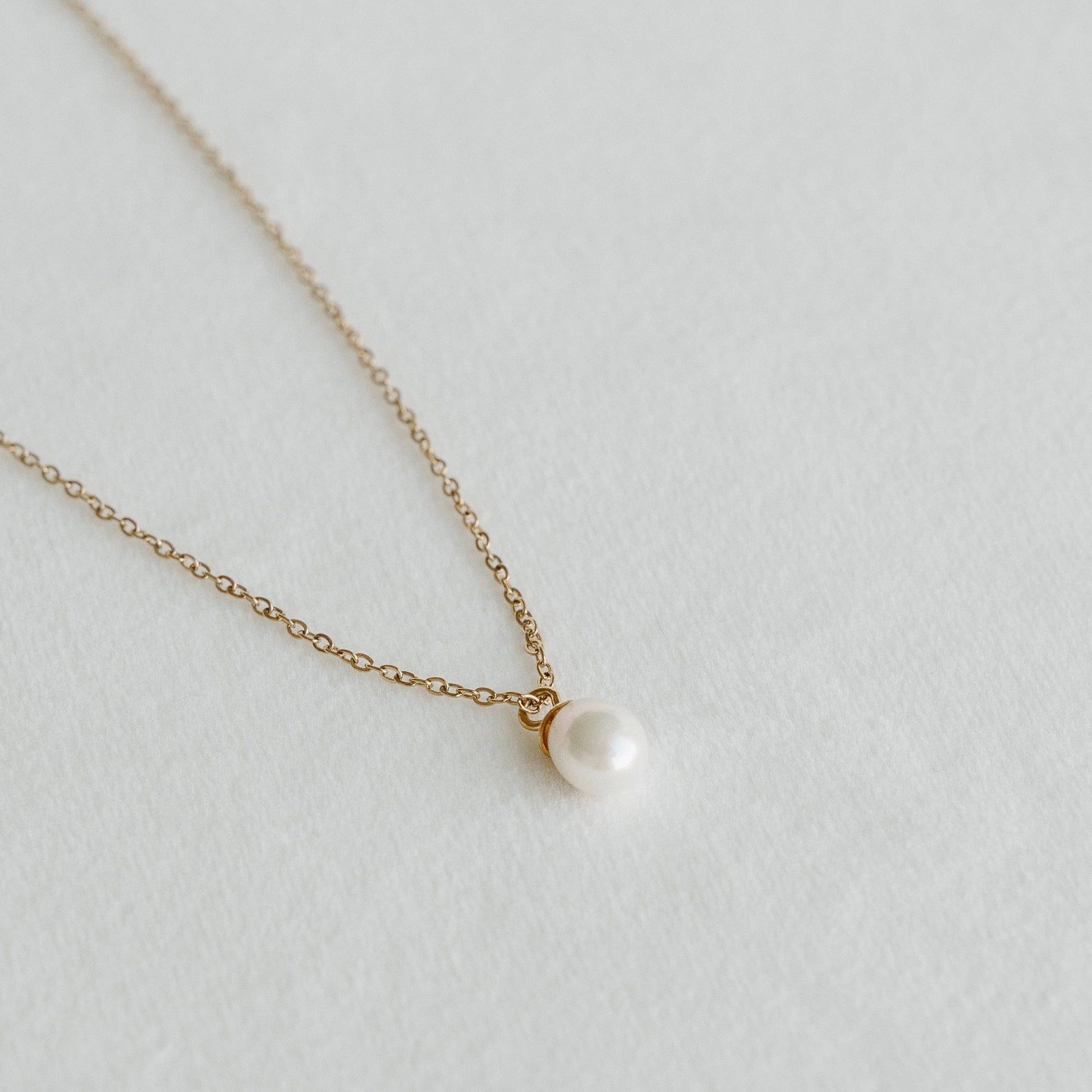 Freshwater pearl pendant on a delicate gold chain necklace laid on a light textured surface - PABOOM