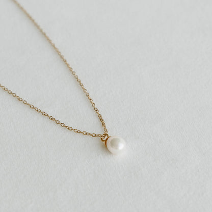 Freshwater pearl pendant on a delicate gold chain necklace laid on a light textured surface - PABOOM