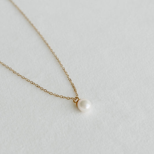 Freshwater pearl pendant on a delicate gold chain necklace laid on a light textured surface - PABOOM