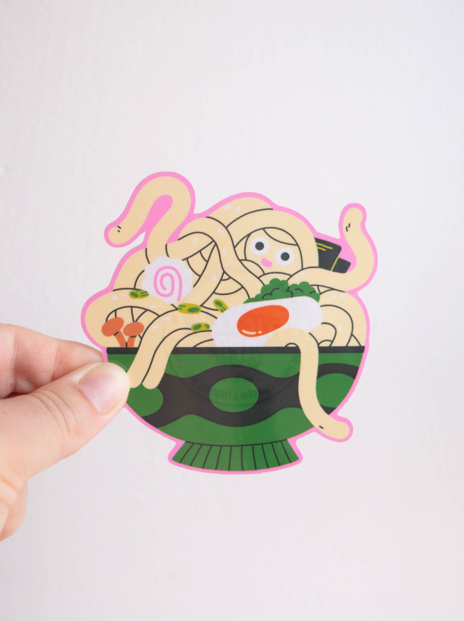 Ramen Vinyl Sticker — illustration of a ramen bowl with noodle limbs and a small peeking face, held between two fingers