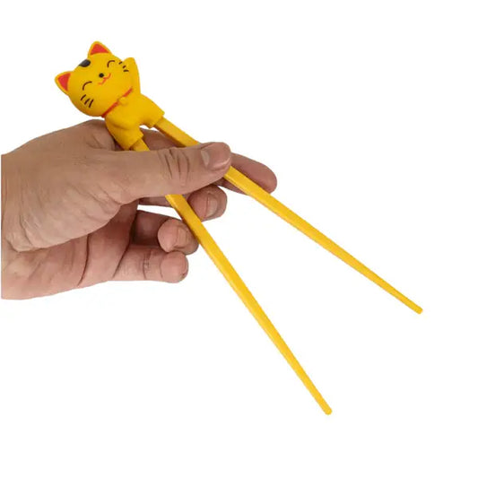 Hand holding yellow lucky cat training chopsticks with a waving maneki-neko topper - PABOOM