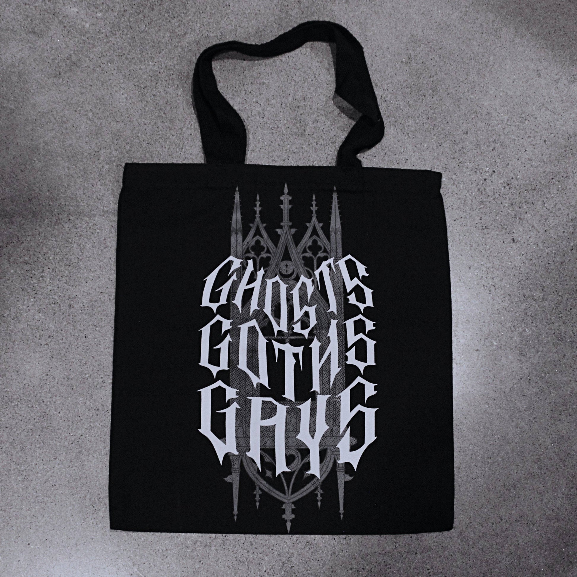 Black cotton canvas tote bag with gothic cathedral-style lettering reading Ghosts, Goths, Gays printed in grey and white across the front