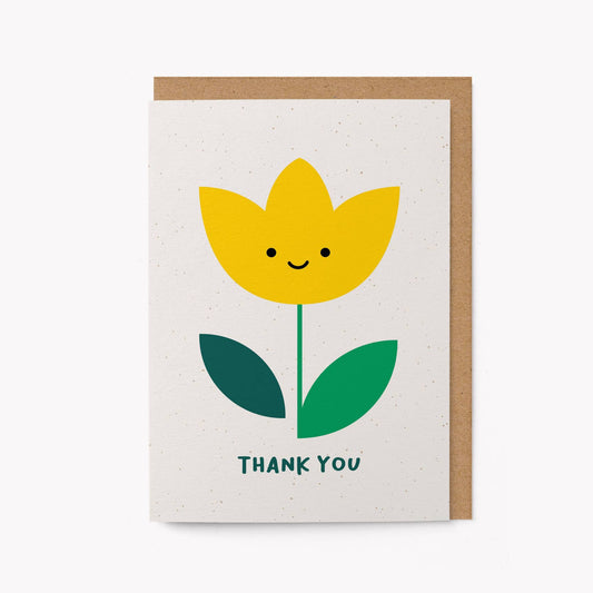 Cream greeting card with an illustrated smiling yellow tulip and the words 'THANK YOU' in green, kraft envelope alongside